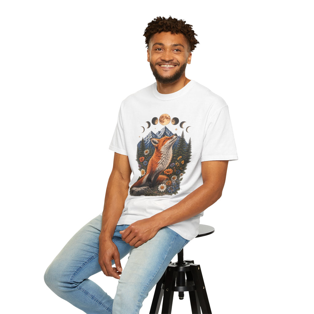 A smiling man with curly hair sits on a black stool wearing a white graphic t-shirt and light blue jeans against a plain white background. The t-shirt features a detailed graphic of a fox surrounded by moon phases, mountains, and flowers.