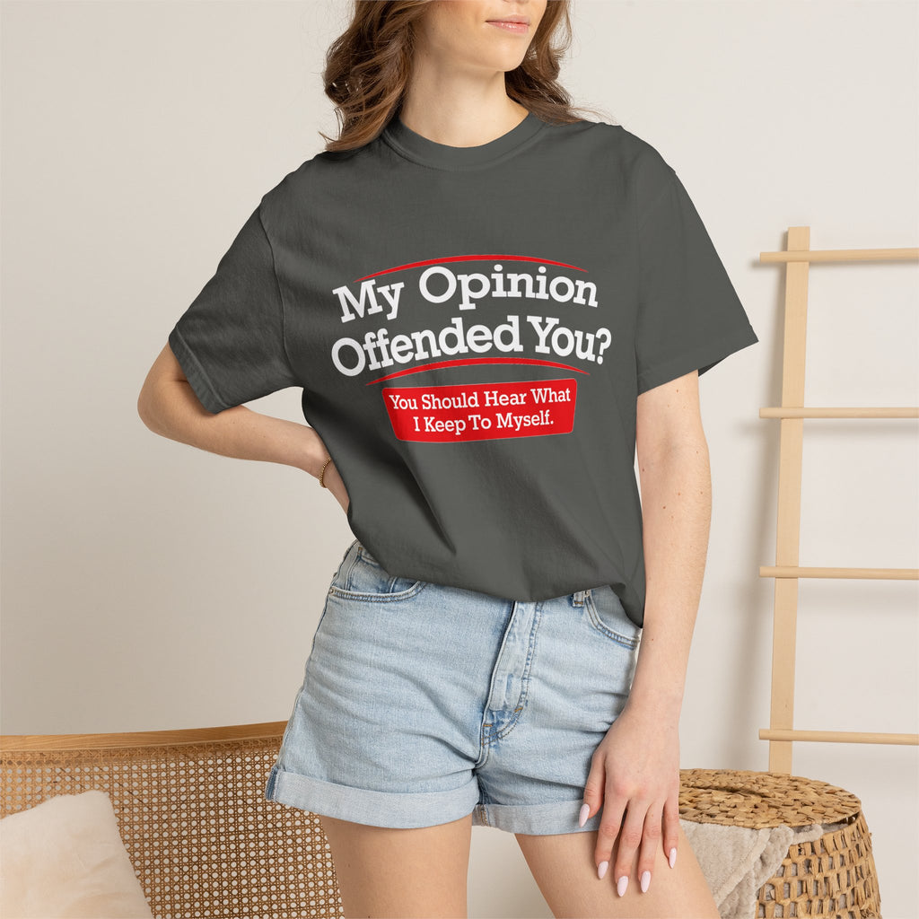 A woman wearing a dark charcoal gray graphic t-shirt with the text 'My Opinion Offended You? You Should Hear What I Keep To Myself!' in white and red, paired with light-wash denim shorts in a neutral indoor setting.