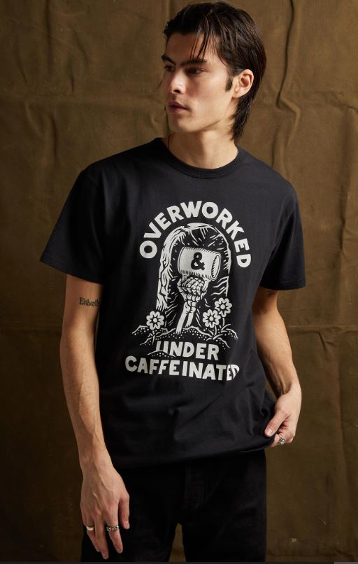 Man wearing funny coffee skeleton t-shirt with Overworked and Undercaffeinated tombstone design, vintage woodcut print on black premium cotton unisex tee for coffee lovers