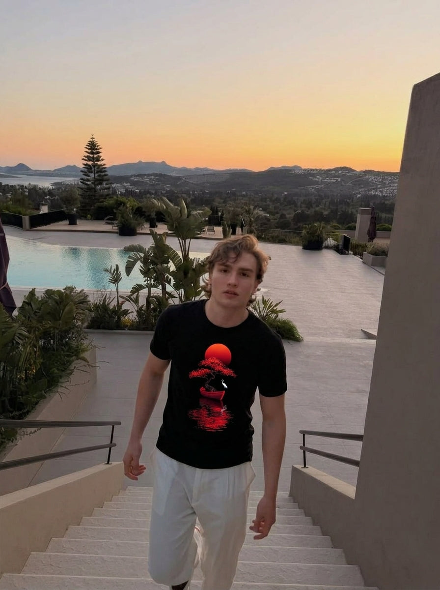 Striking red bonsai and rising sun graphic tee with Japanese-inspired art. Premium heavyweight cotton, unisex fit. Free shipping across the US & Europe. Man wearing black t-shirt with red bonsai tree in a boat under a rising sun and white heron, minimalist Japanese art print on premium cotton unisex tee